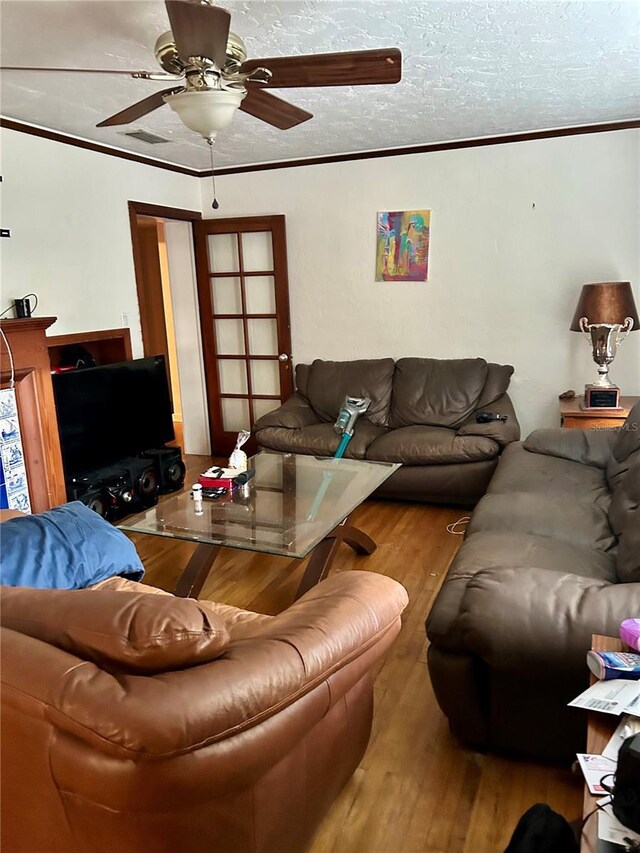 living room featuring wood-type flooring, a textured ceiling, ceiling fan, and crown molding