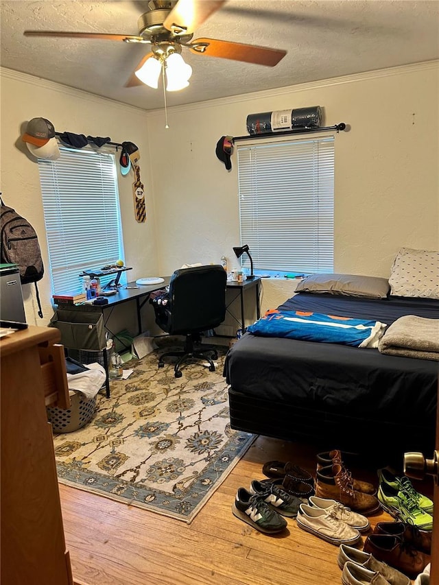 bedroom featuring a textured ceiling, hardwood / wood-style flooring, ceiling fan, and ornamental molding