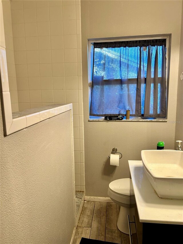 bathroom with hardwood / wood-style floors, toilet, a tile shower, and vanity