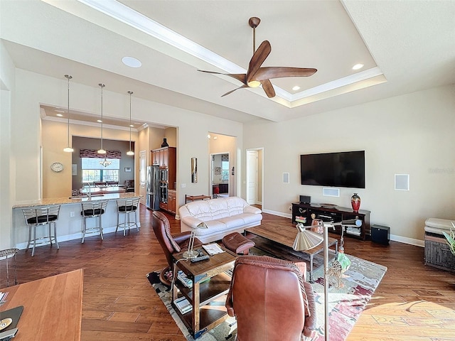 living room featuring a raised ceiling, ceiling fan, crown molding, and dark wood-type flooring