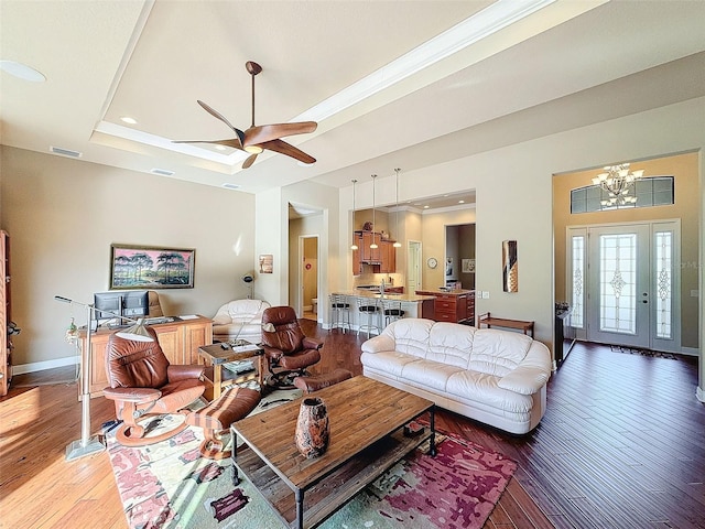 living room with ceiling fan with notable chandelier, dark hardwood / wood-style floors, and a tray ceiling