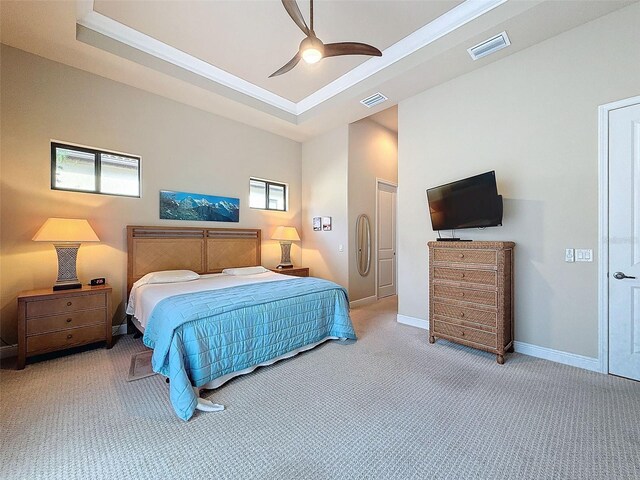 bedroom with ceiling fan, light colored carpet, multiple windows, and a tray ceiling