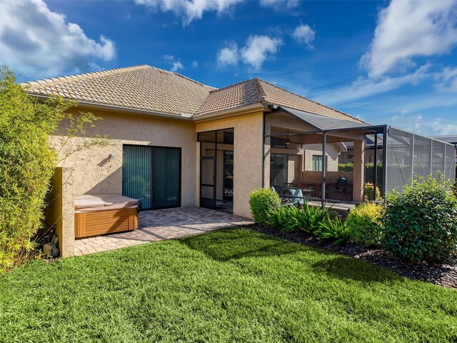 back of house with a lawn, glass enclosure, a patio area, and a hot tub