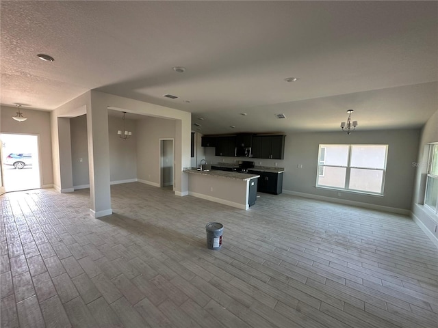 unfurnished living room with a textured ceiling, a notable chandelier, sink, and light hardwood / wood-style flooring