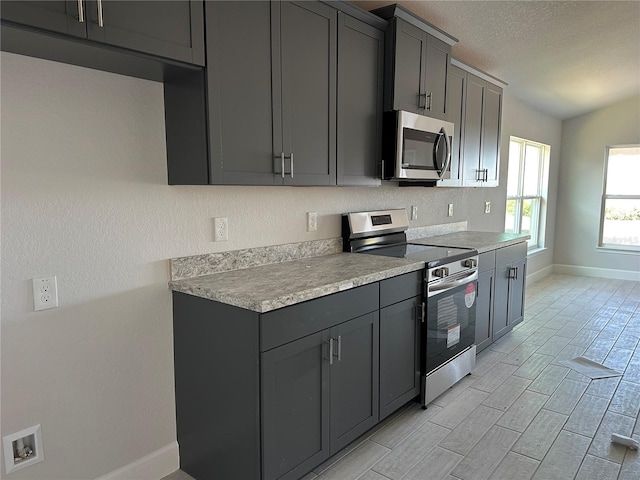 kitchen featuring a textured ceiling, gray cabinets, stainless steel appliances, and vaulted ceiling