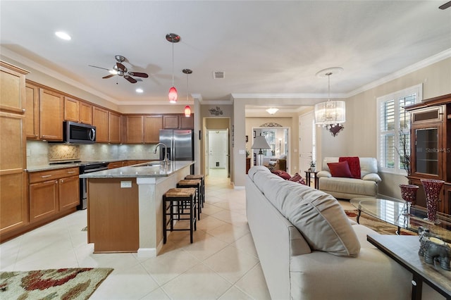 kitchen featuring a kitchen island with sink, stainless steel appliances, decorative light fixtures, and ornamental molding