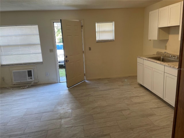 kitchen with white cabinets, light stone counters, a wall mounted AC, and sink