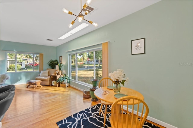 sitting room with hardwood / wood-style floors, a skylight, an inviting chandelier, and plenty of natural light