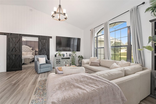 living room with a barn door, an inviting chandelier, vaulted ceiling, and light wood-type flooring