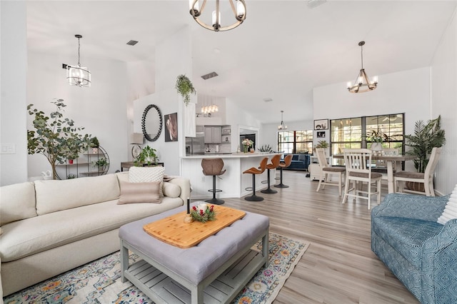 living room with light hardwood / wood-style flooring, a towering ceiling, and a notable chandelier