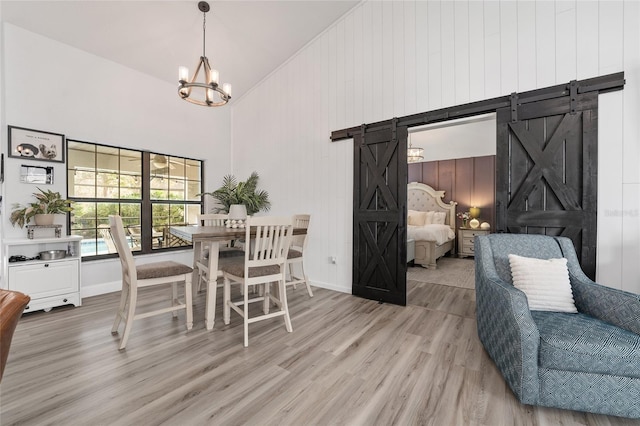 dining area with wood-type flooring, a barn door, high vaulted ceiling, a chandelier, and wood walls