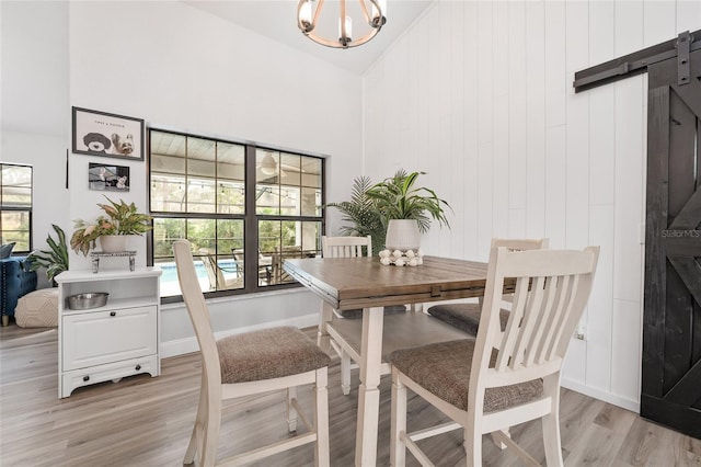 dining space with an inviting chandelier, a barn door, light hardwood / wood-style flooring, high vaulted ceiling, and wooden walls