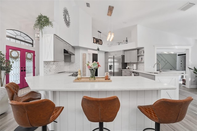 kitchen featuring kitchen peninsula, stainless steel fridge, gray cabinetry, high vaulted ceiling, and light hardwood / wood-style floors