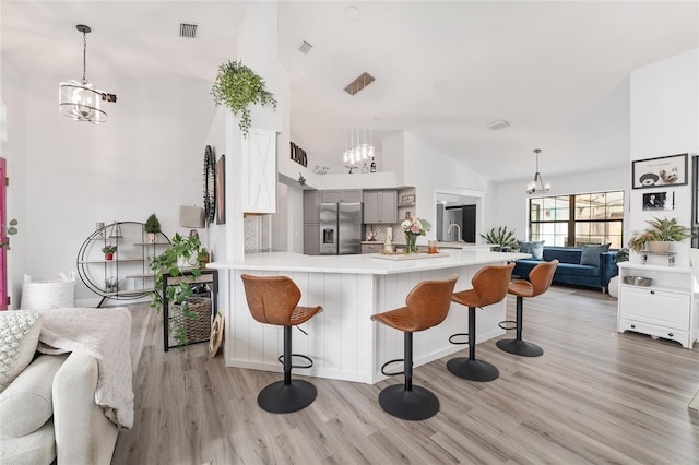 kitchen featuring kitchen peninsula, stainless steel fridge, light wood-type flooring, a kitchen breakfast bar, and gray cabinets