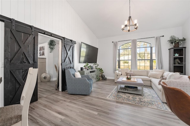 living room featuring a barn door, light hardwood / wood-style flooring, a chandelier, and vaulted ceiling