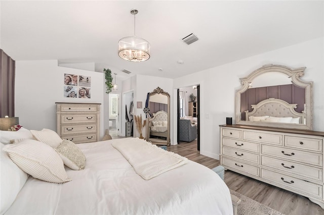 bedroom with light hardwood / wood-style floors, vaulted ceiling, and an inviting chandelier