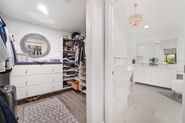 spacious closet featuring light hardwood / wood-style flooring and an inviting chandelier