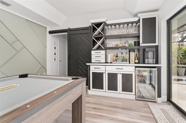 bar featuring a barn door, light hardwood / wood-style floors, white cabinetry, and beverage cooler