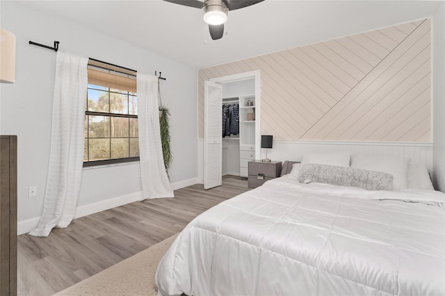 bedroom featuring ceiling fan, light hardwood / wood-style flooring, wood walls, a walk in closet, and a closet