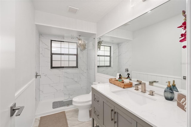 bathroom with a tile shower, vanity, and toilet