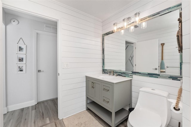 bathroom with vanity, wooden walls, crown molding, hardwood / wood-style flooring, and toilet