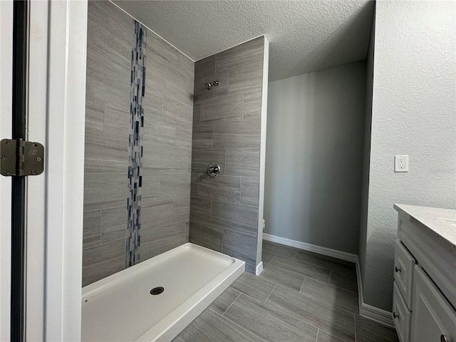 bathroom with toilet, vanity, a textured ceiling, and tiled shower