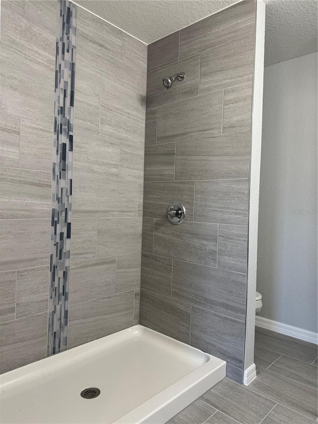 bathroom with toilet, a textured ceiling, and a tile shower