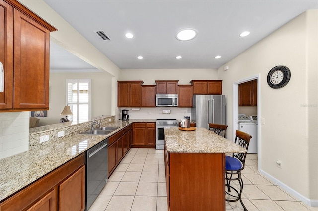 kitchen featuring a kitchen bar, appliances with stainless steel finishes, kitchen peninsula, sink, and independent washer and dryer