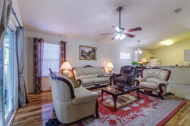 living room featuring hardwood / wood-style floors, ceiling fan with notable chandelier, a wealth of natural light, and lofted ceiling