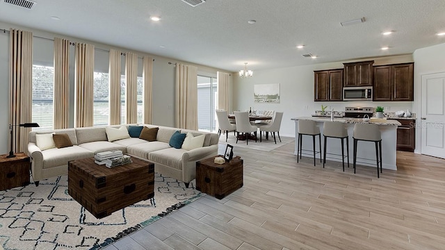 living room featuring a textured ceiling, light wood-type flooring, and an inviting chandelier