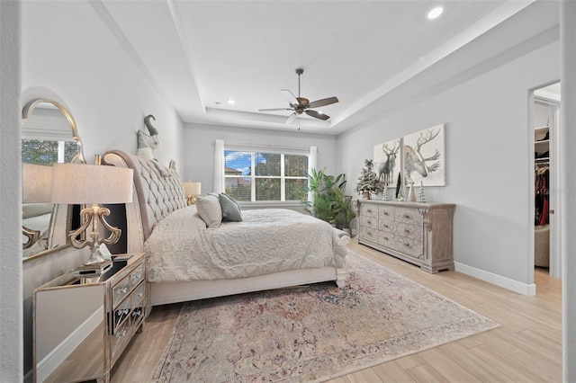 bedroom featuring ceiling fan, a raised ceiling, light wood-type flooring, and multiple windows