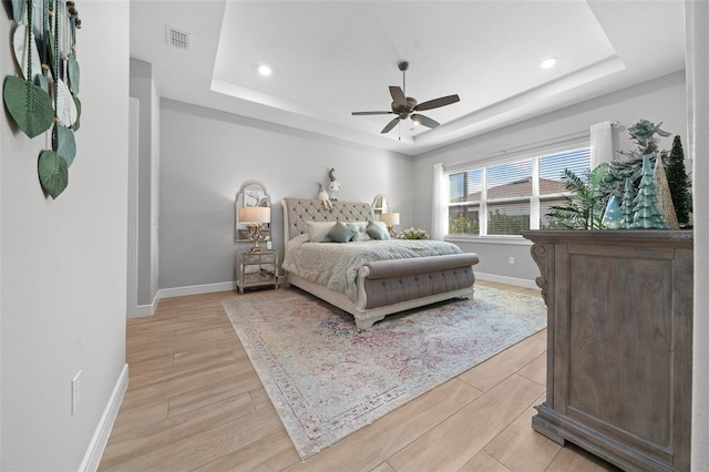 bedroom featuring light wood-type flooring, a raised ceiling, and ceiling fan