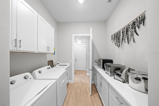 clothes washing area with light hardwood / wood-style floors, cabinets, sink, and washing machine and dryer