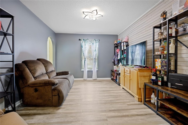 living room with a textured ceiling, light wood-type flooring, and wood walls