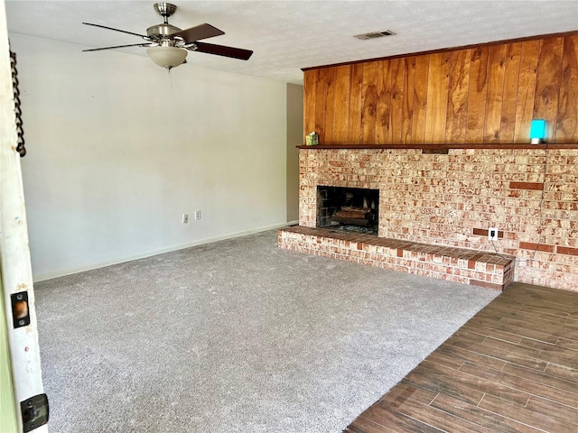 unfurnished living room featuring a textured ceiling, wooden walls, a fireplace, and dark hardwood / wood-style floors