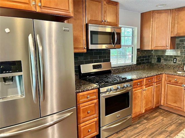 kitchen featuring backsplash, a textured ceiling, stainless steel appliances, dark stone countertops, and hardwood / wood-style floors