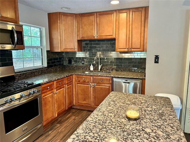 kitchen with sink, dark hardwood / wood-style floors, dark stone countertops, a textured ceiling, and appliances with stainless steel finishes