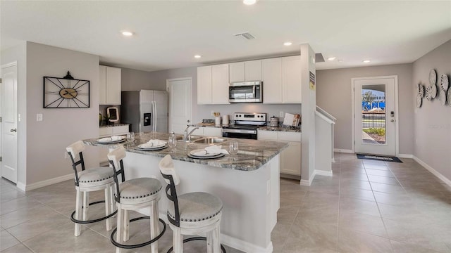 kitchen with dark stone counters, white cabinets, sink, an island with sink, and stainless steel appliances