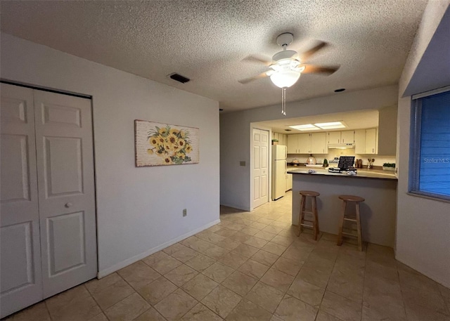 kitchen with white fridge, stove, kitchen peninsula, a textured ceiling, and white cabinets