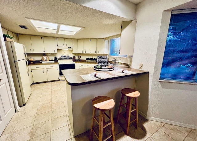 kitchen featuring white fridge, kitchen peninsula, a kitchen breakfast bar, stove, and a textured ceiling