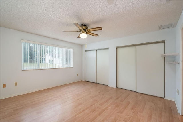 unfurnished bedroom featuring ceiling fan, multiple closets, light wood-type flooring, and a textured ceiling