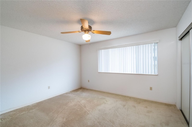 spare room featuring a textured ceiling, ceiling fan, and light colored carpet