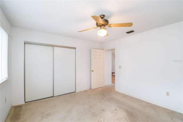 unfurnished bedroom featuring ceiling fan, light colored carpet, a textured ceiling, and a closet