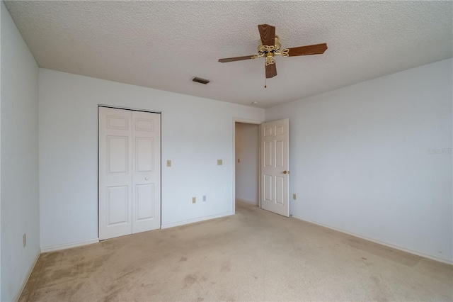 unfurnished bedroom with ceiling fan, a textured ceiling, a closet, and light carpet