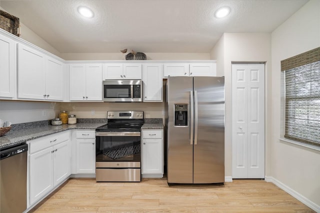 kitchen featuring white cabinets, light wood-type flooring, appliances with stainless steel finishes, and dark stone countertops