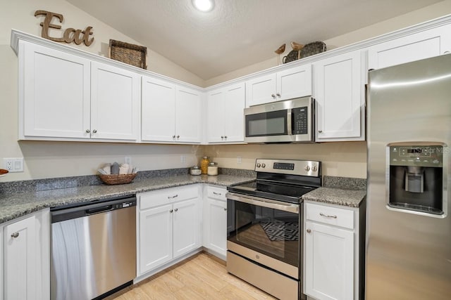 kitchen featuring white cabinets, appliances with stainless steel finishes, light hardwood / wood-style floors, stone countertops, and vaulted ceiling