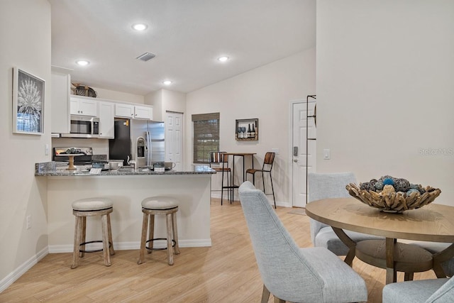 kitchen featuring white cabinetry, a kitchen bar, kitchen peninsula, appliances with stainless steel finishes, and light stone counters