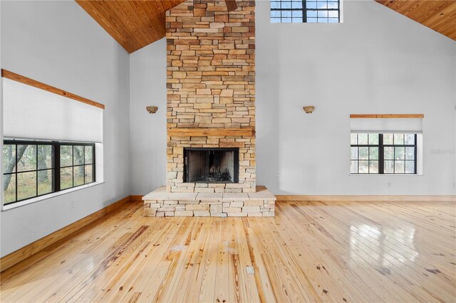 unfurnished living room with light hardwood / wood-style floors, a stone fireplace, wooden ceiling, and high vaulted ceiling