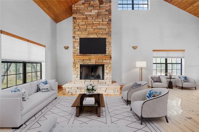 living room featuring light hardwood / wood-style flooring, high vaulted ceiling, wooden ceiling, and a stone fireplace