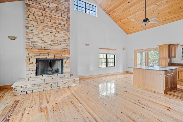 kitchen with a high ceiling, a stone fireplace, light hardwood / wood-style flooring, a kitchen island, and wood ceiling